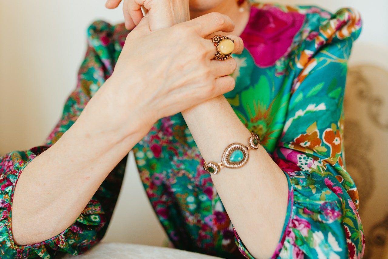 A woman sitting at a table wears a turquoise gemstone bracelet and a colorful top