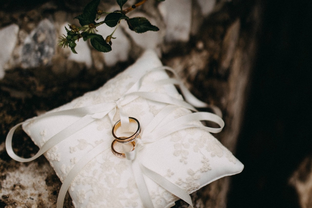Two wedding bands tied with ribbons and sitting on a white pillow