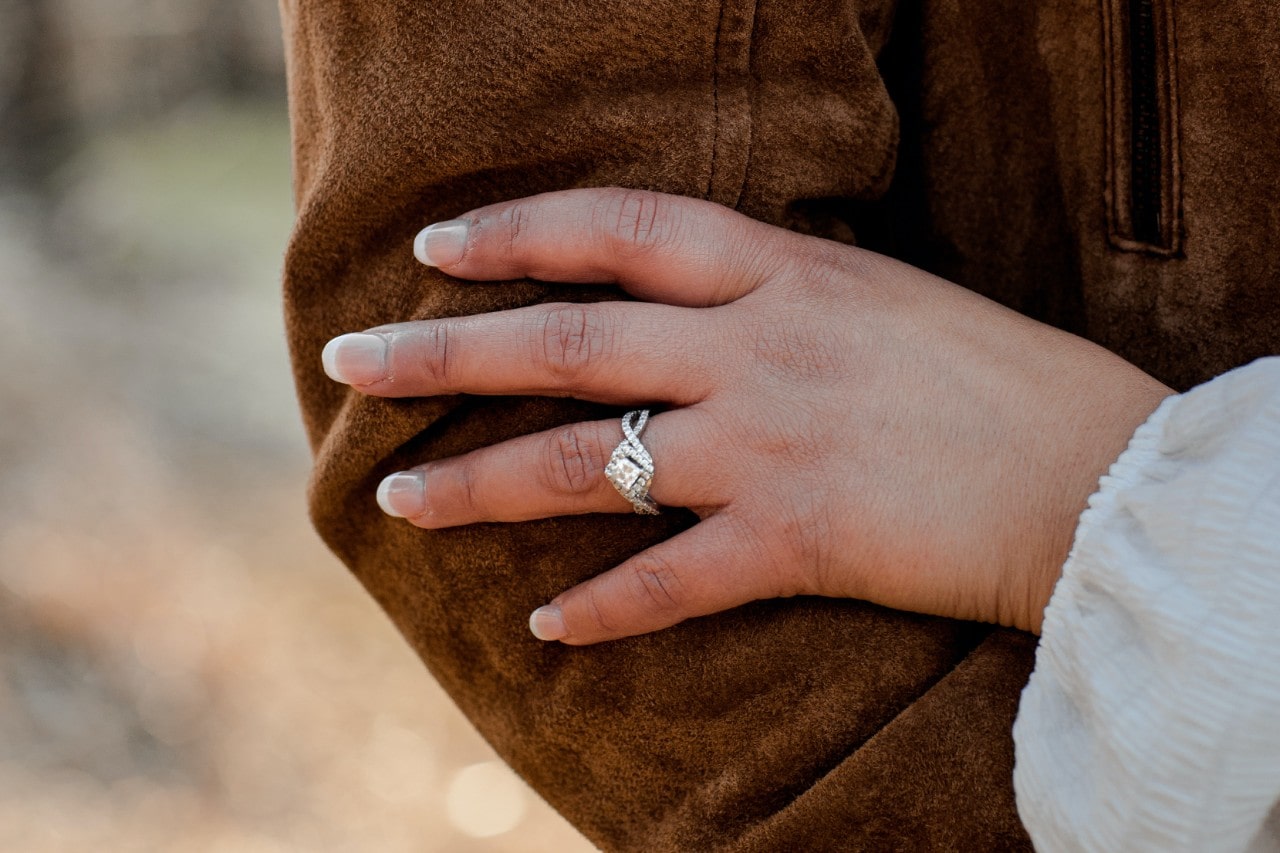 Woman’s hand resting on her partner’s arm, wearing a princess cut engagement ring