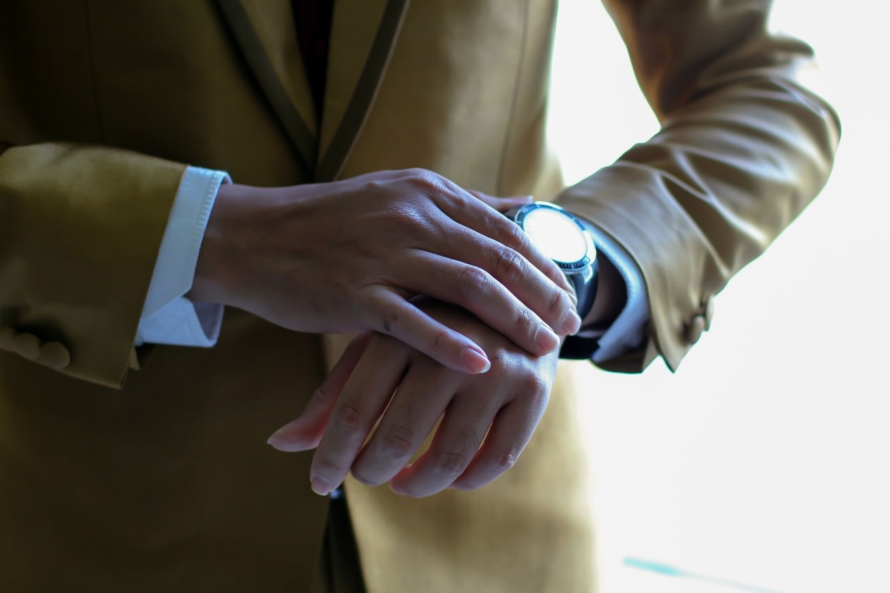 Man wearing a beige suit and looking at his watch