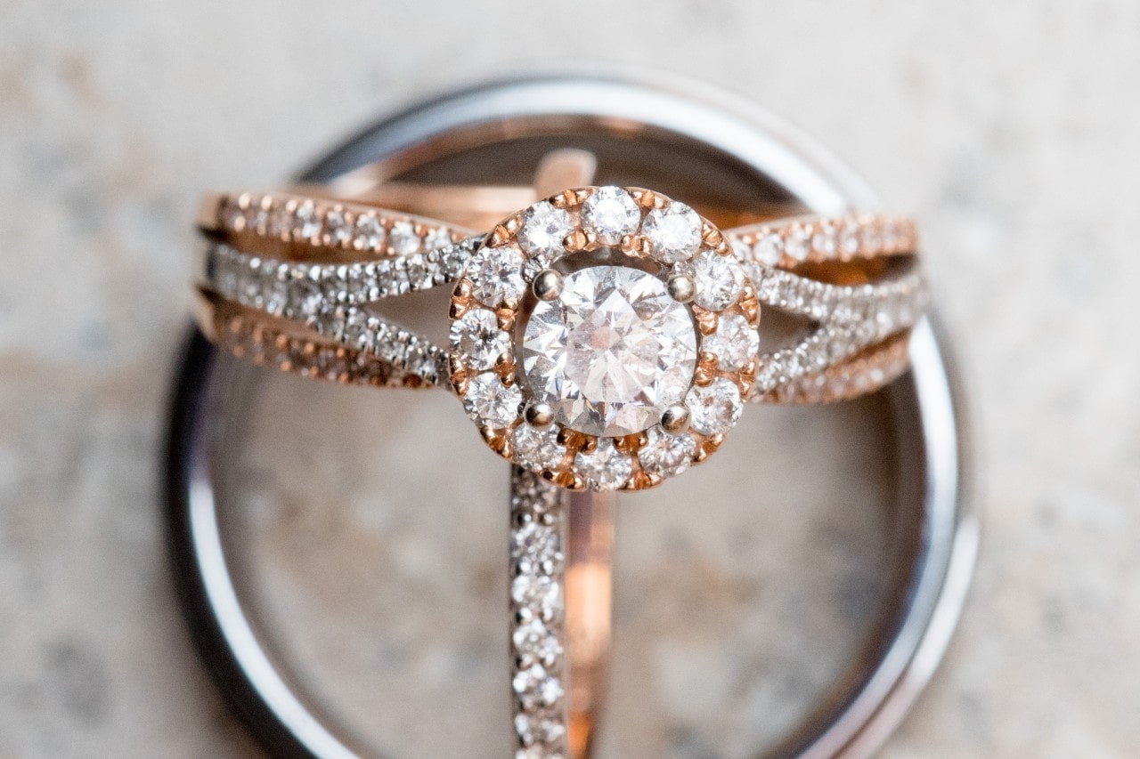 a white gold and rose gold halo engagement ring sits with two wedding bands.