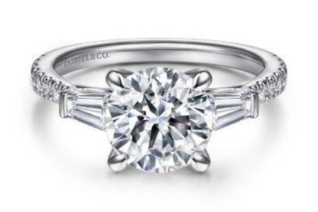 A three stone engagement ring with a round cut diamond and two baguette diamonds.