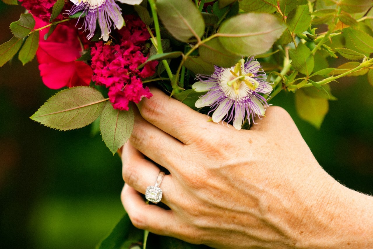 A woman holding a bouquet of flowers wearing a cushion-cut halo engagement ring.