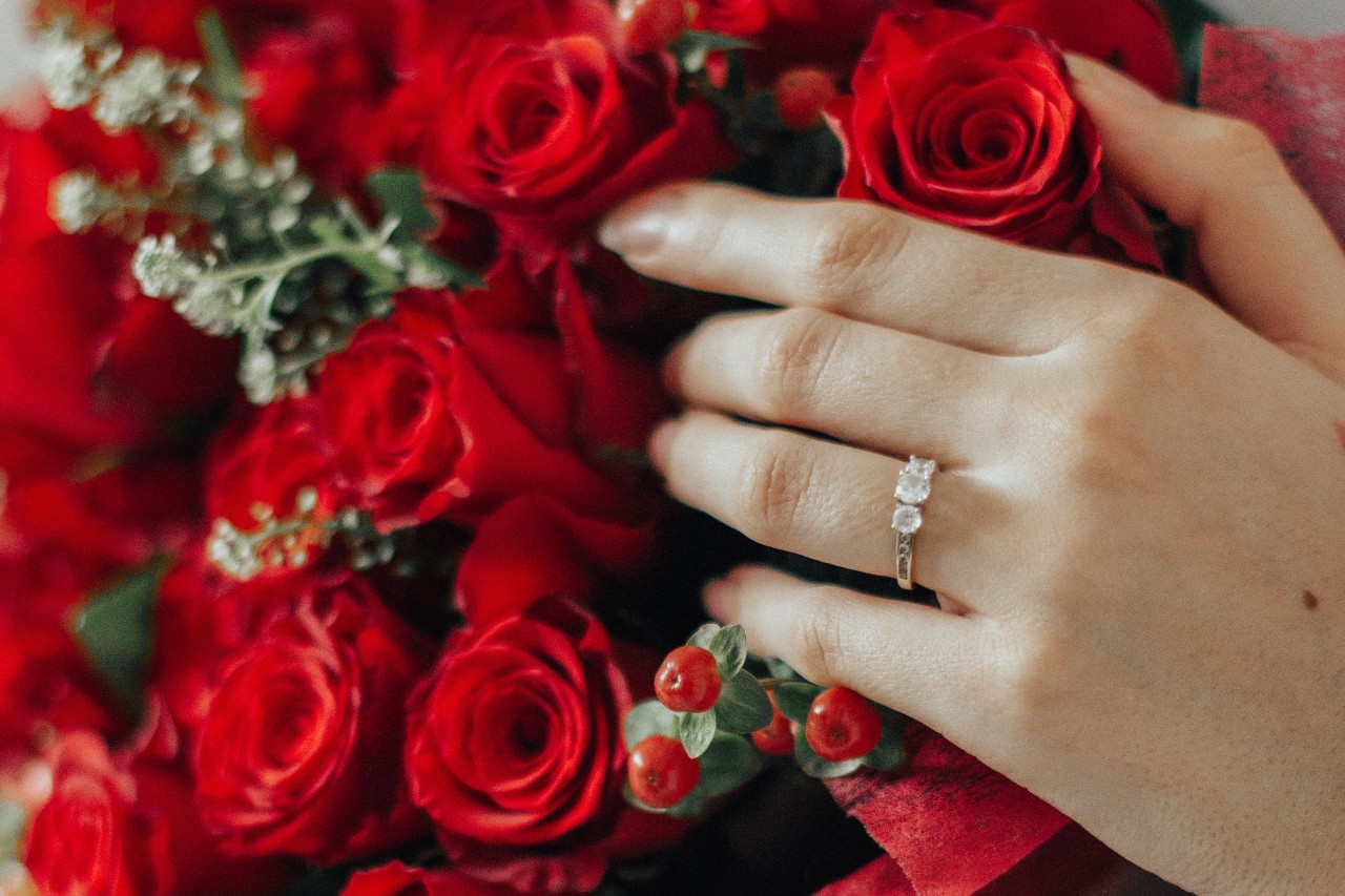 A hand with a three stone engagement ring resting on a bouquet of red roses