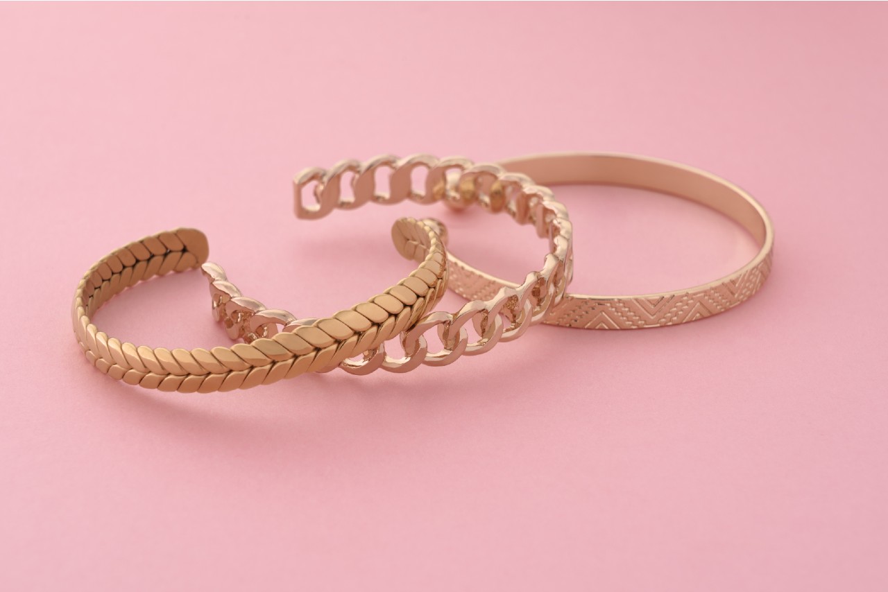 Three rose gold bracelets sitting on a pink, spring-appropriate pastel background