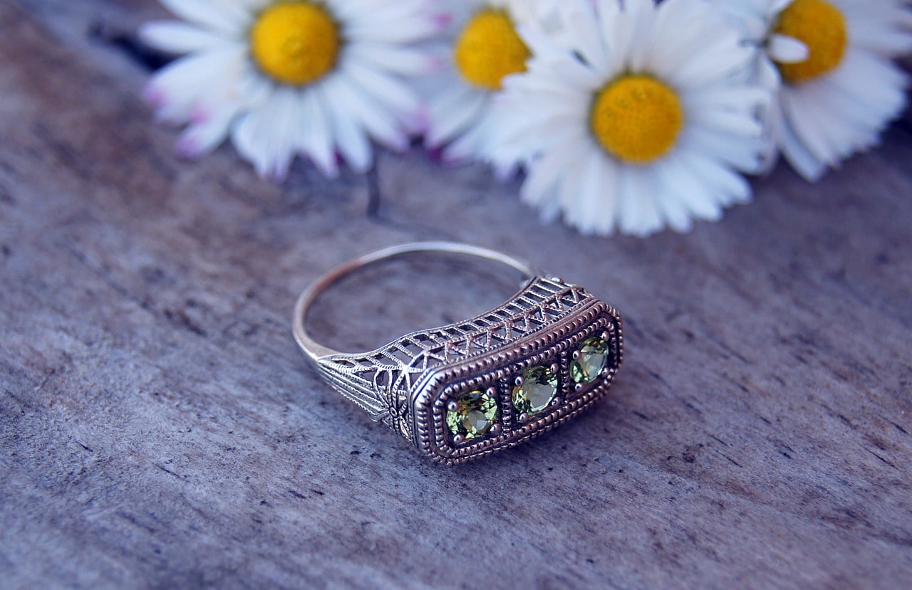 A vintage-inspired peridot fashion ring sits on a wooden surface with daisies