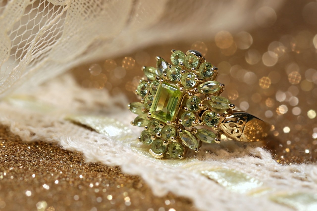 A gold peridot halo fashion ring sitting on gold glitter and lace