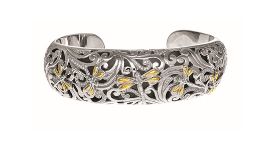 A silver cuff bracelet with an elaborately engraved design featuring dragonflies with gold wings