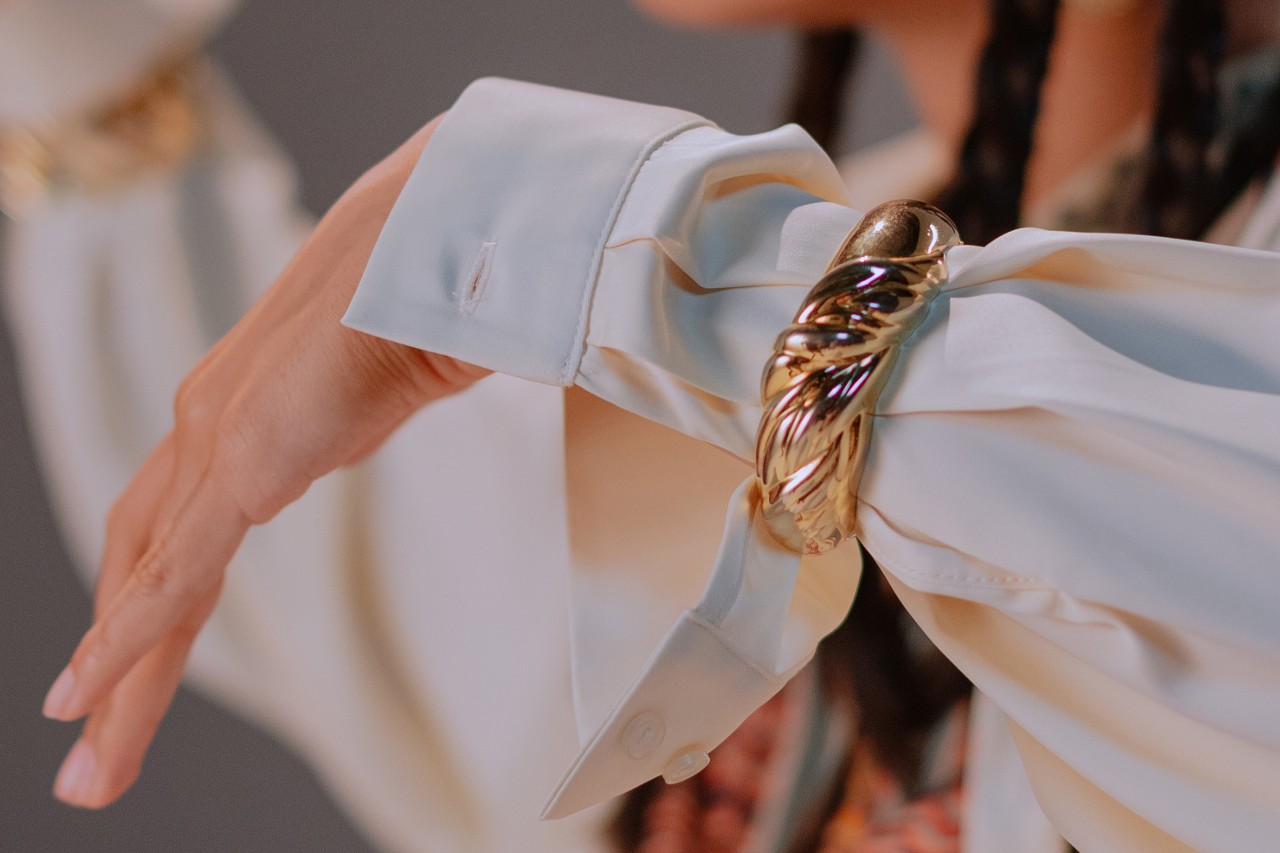 Close up image of a woman wearing a long sleeve white top and a chunky gold bracelet
