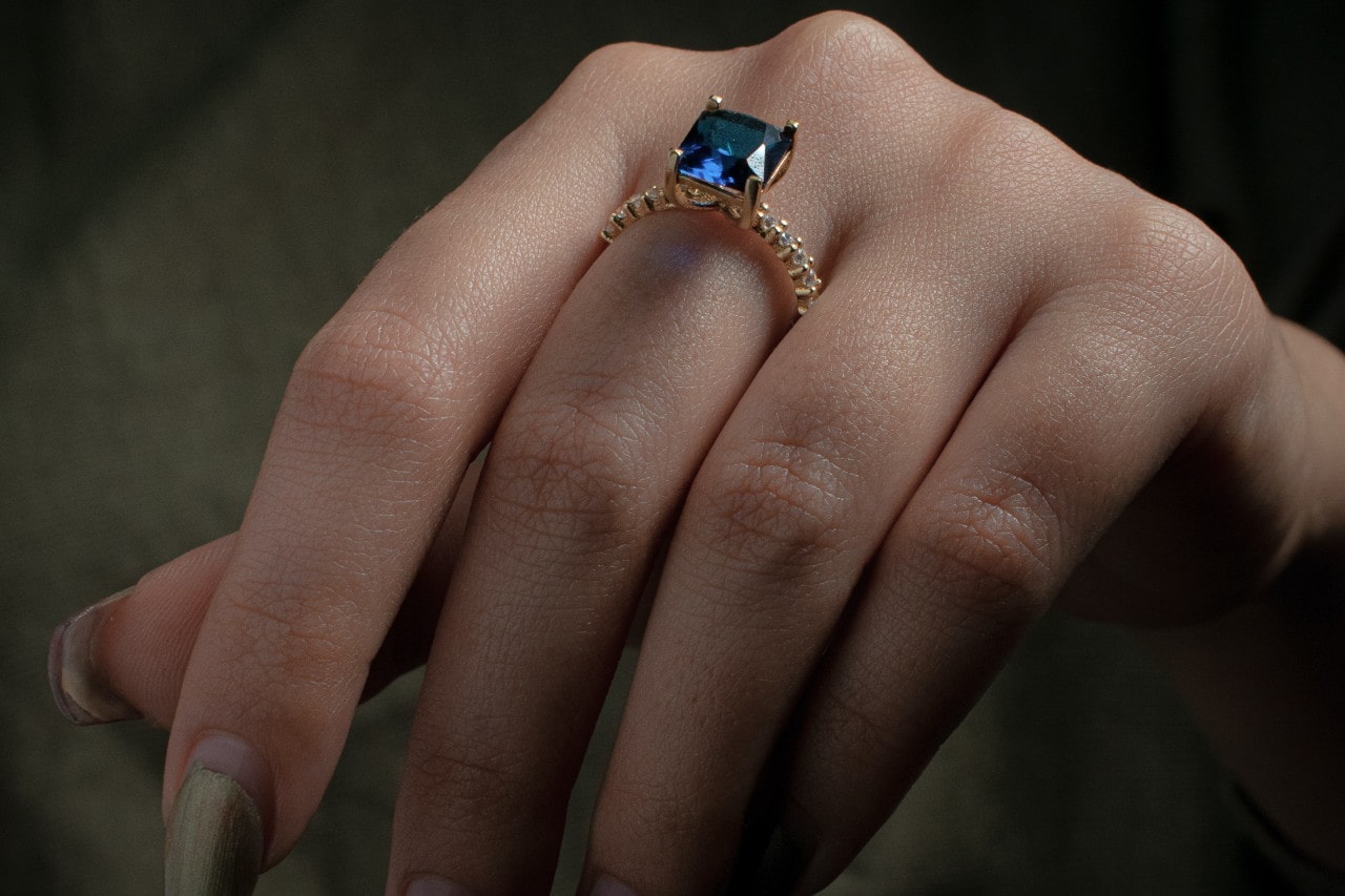 Close up image of a hand wearing a sapphire fashion ring set in yellow gold