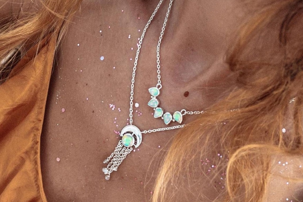 Close up image of a woman’s chest adorned with glitter and two opal necklaces