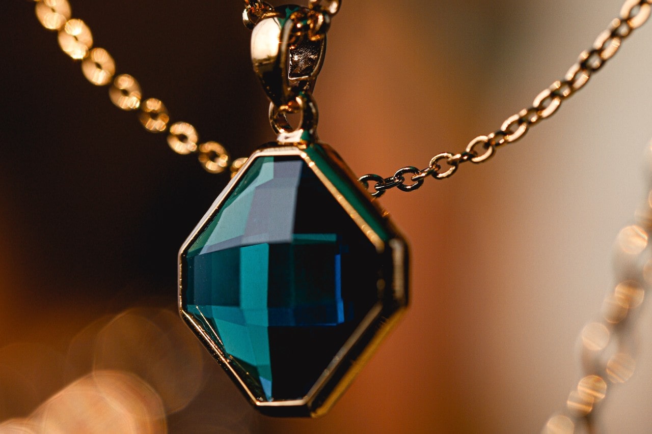 close up image of a pendant necklace with a deep blue green gemstone