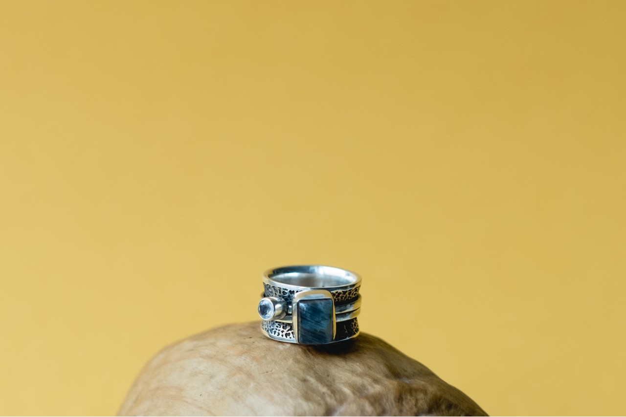 A blue topaz and white gold fashion ring sits on a wooden pedestal in front of a yellow wall.