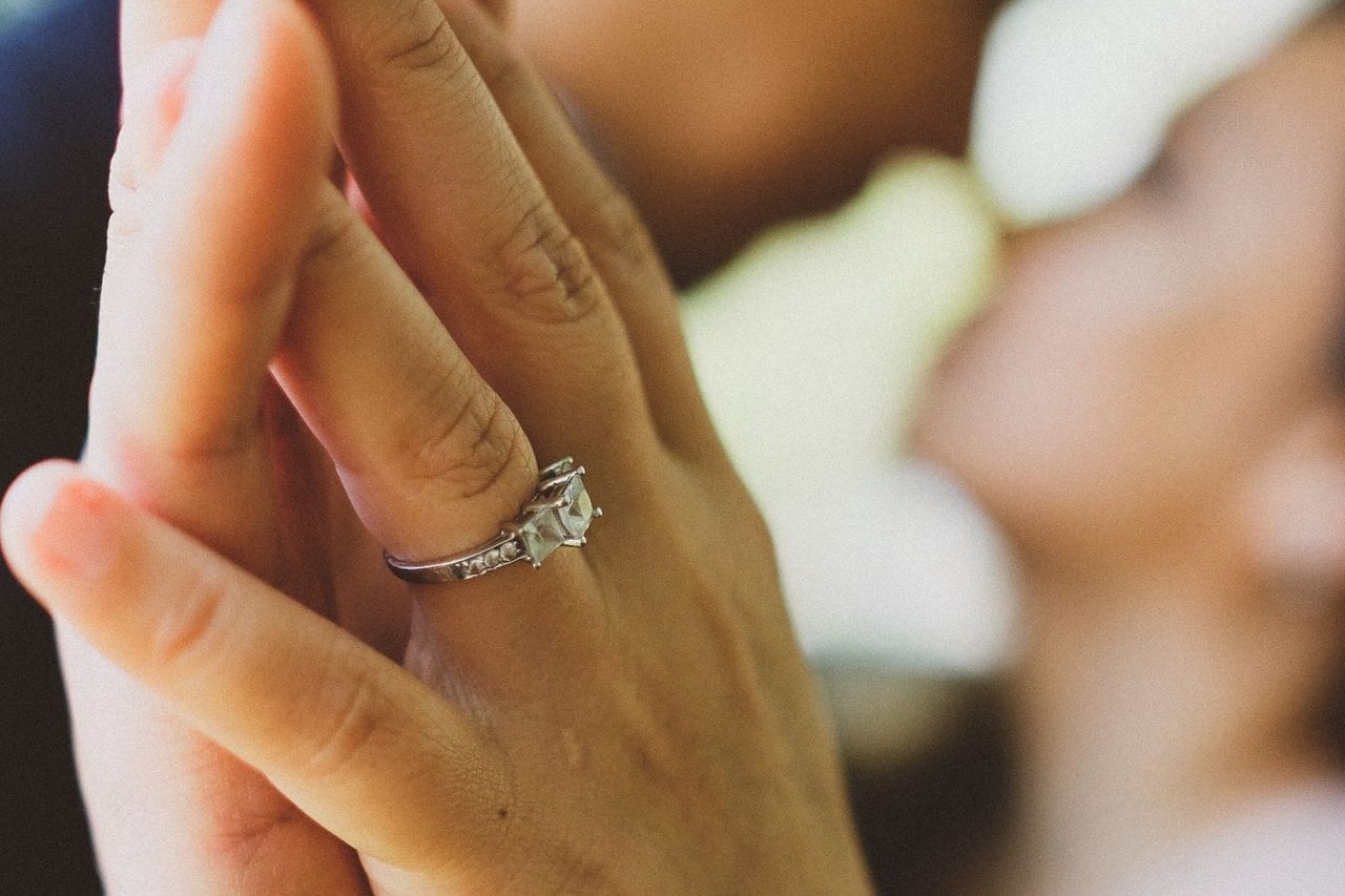 A couple embraces, holding hands while showing off a three-stone engagement ring.