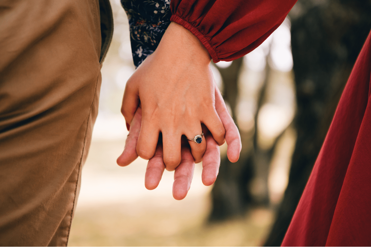 A couple holds hands, the woman wearing a sapphire engagement ring.