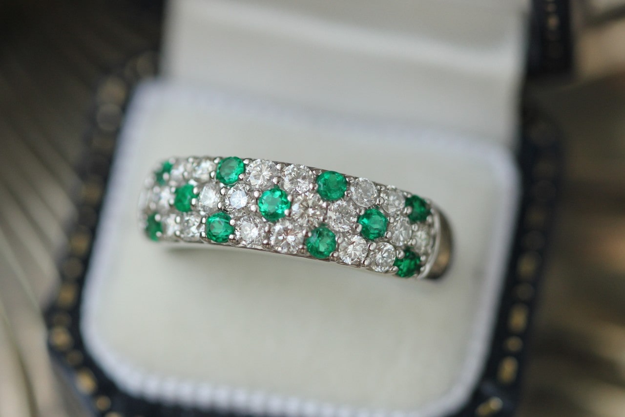 Ring box containing a pave wedding band set with diamonds and emeralds
