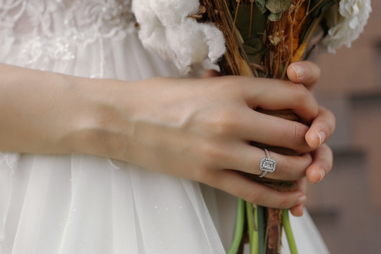 Bride holding her wedding bouquet and wearing a halo, emerald cut engagement ring