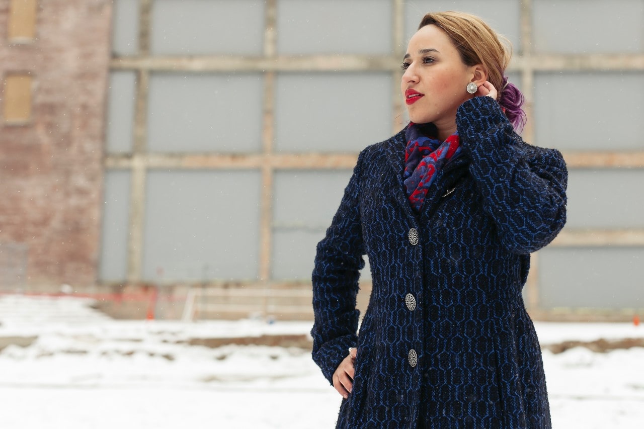 a woman in the winter scratches her ear, showing off her platinum earrings.