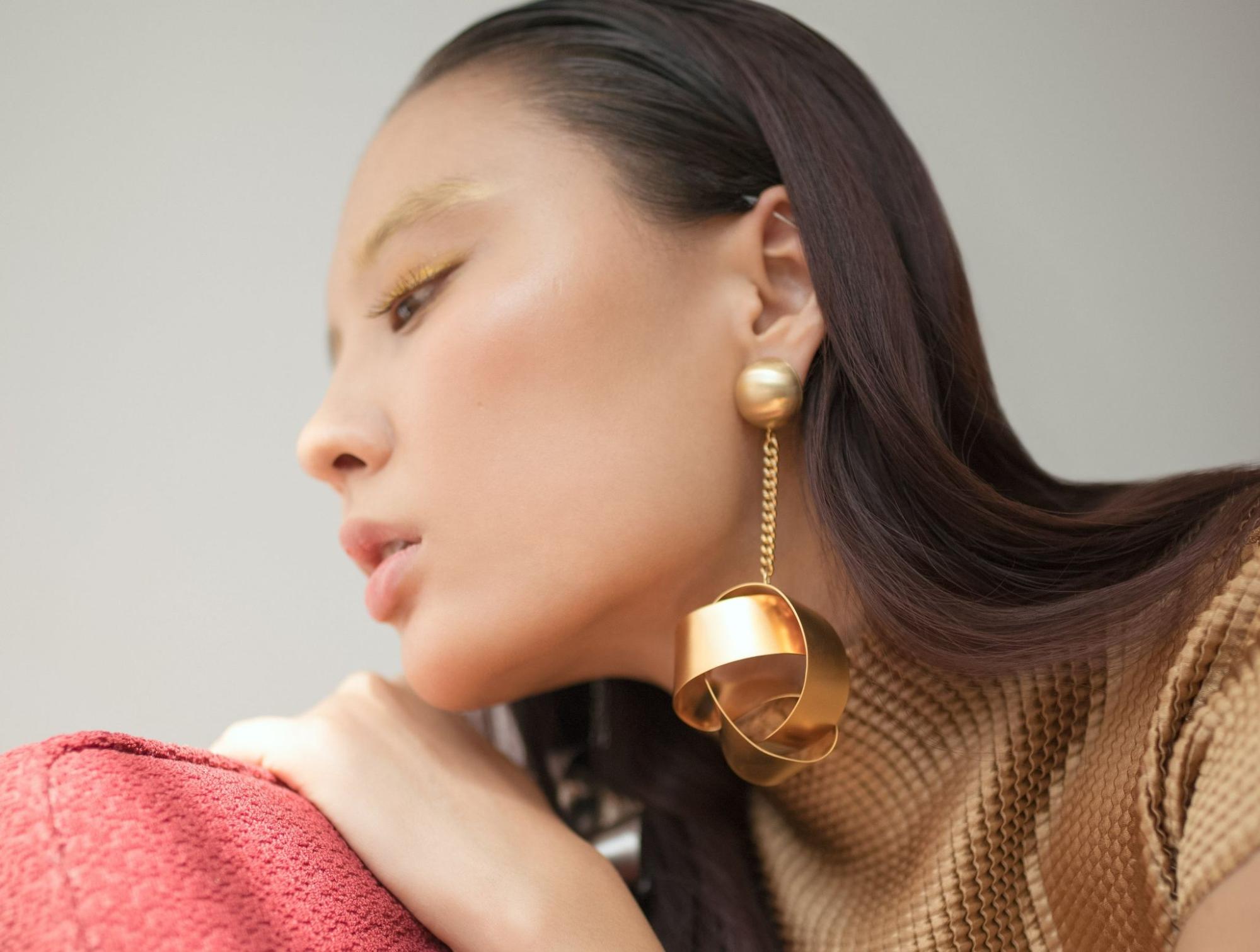A woman wearing a dramatic drop earring leans on a red couch.