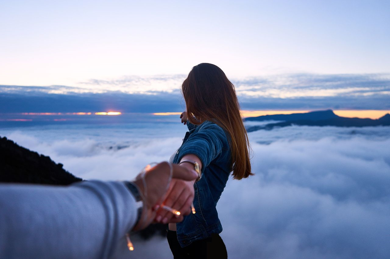 A bride and groom to-be holding hands overlooking the clouds 