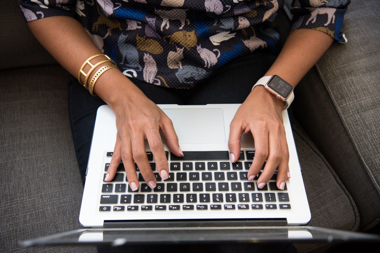 A woman typing on a laptop wearing gold bangles and a smart watch.