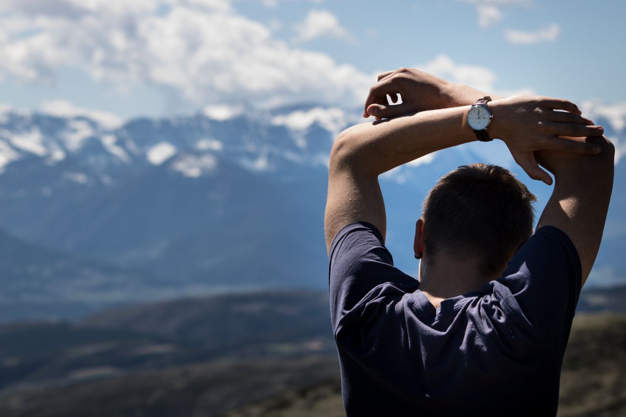 Athletic man standing outside and wearing a watch with a mountain background