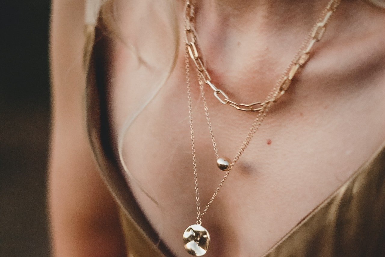 A closeup of a woman's chest that showcases three gold necklaces