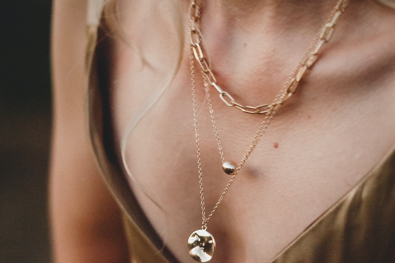 A closeup of a woman's chest that showcases three gold necklaces A closeup of a woman's chest that showcases three gold necklaces