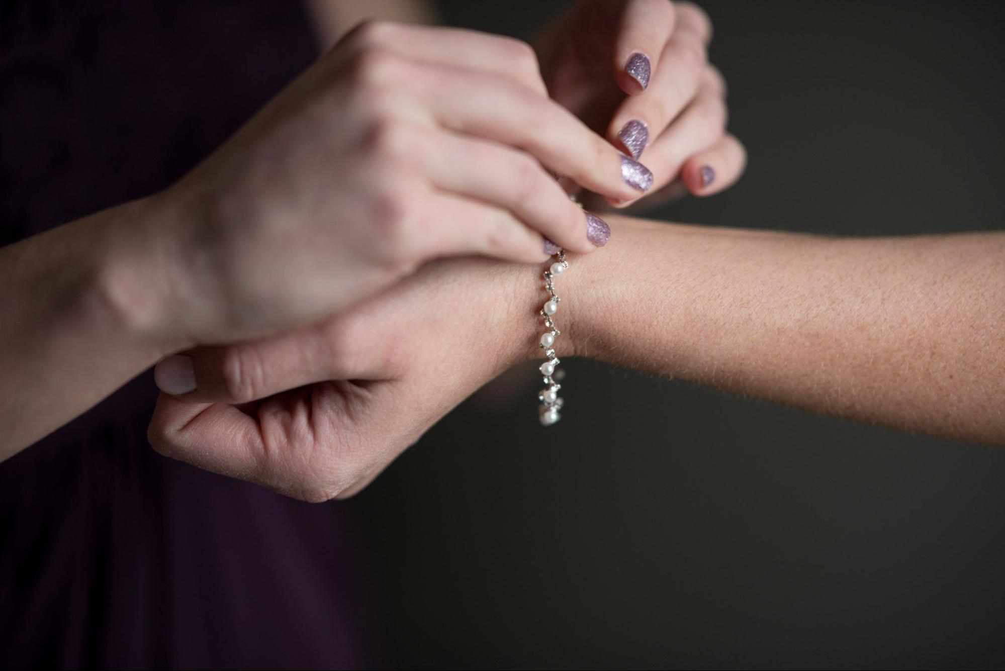 A woman fastens a pearl bracelet around her friend's wrist