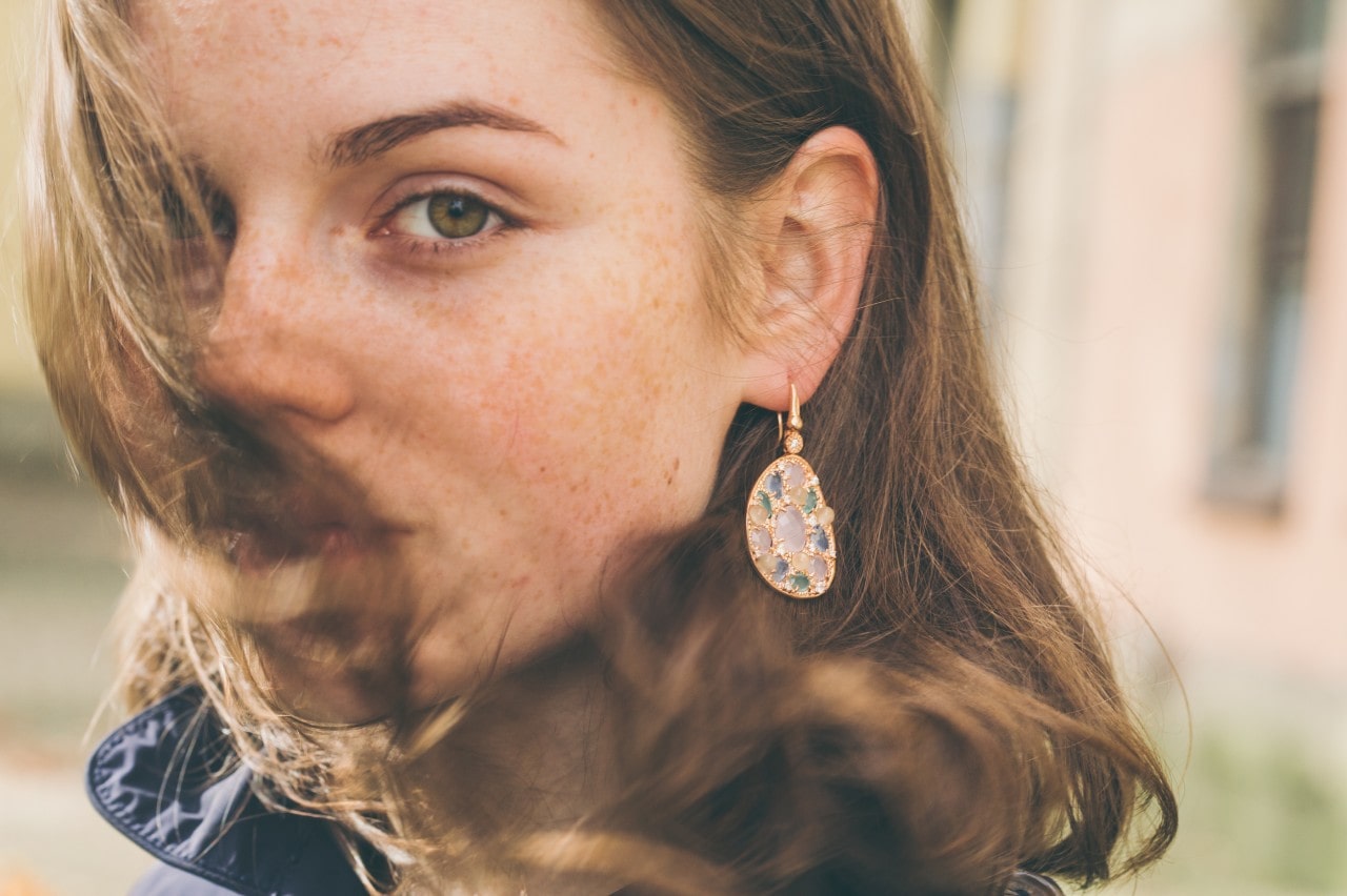A woman wearing gemstone drop earrings looks back as the wind blows A woman wearing gemstone drop earrings looks back as the wind blows